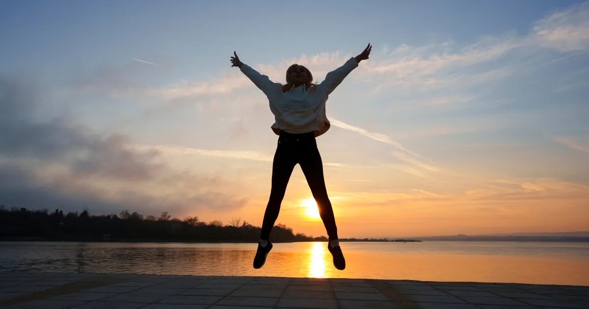 夕日を背にその場でジャンプして喜びを表現している女性。無事退職できた嬉しさと開放感を表している