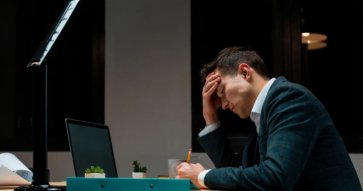 夜のオフィスで一人頭を抱えるビジネスマン。会社を辞めたいが、退職代行を使おうか、苦悩している