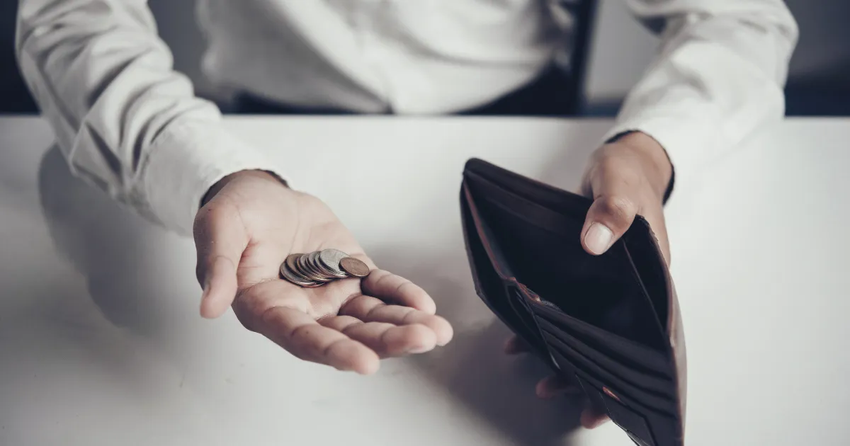 財布から、残った小銭を出している男性。貯金ができずに毎月苦しい思いをしている