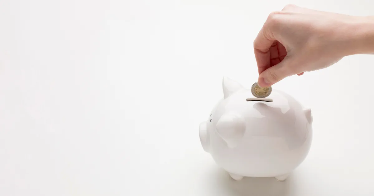 ブタの貯金箱に小銭を入れている人の手。毎日の貯金を習慣化している