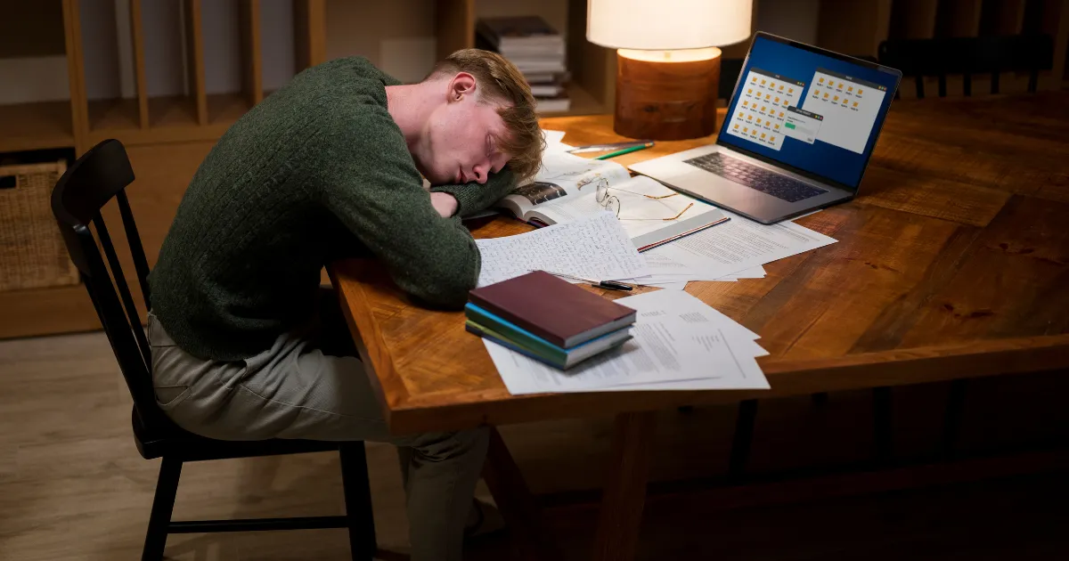 パソコンを開いたままデスクで眠ってしまう男性。本業の合間にwebライターの副業をしており、疲れて眠ってしまっている