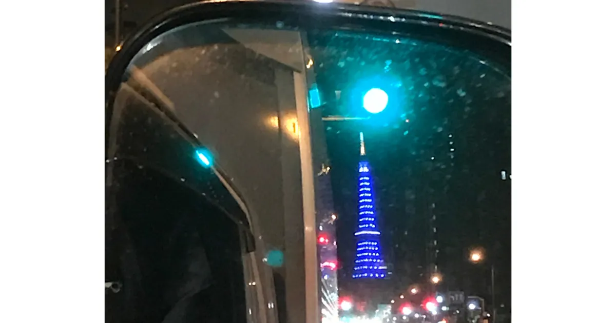 深夜の国道を走る4トントラックの運転席から撮影されたサイドミラーの画像。ミラーには街灯や青い光、後続車のライトが映り込み、ドライバーの腕がわずかに見える。40代で管理職に挫折し、トラックドライバーとして再起した男の孤独だが自由な視点を象徴している。